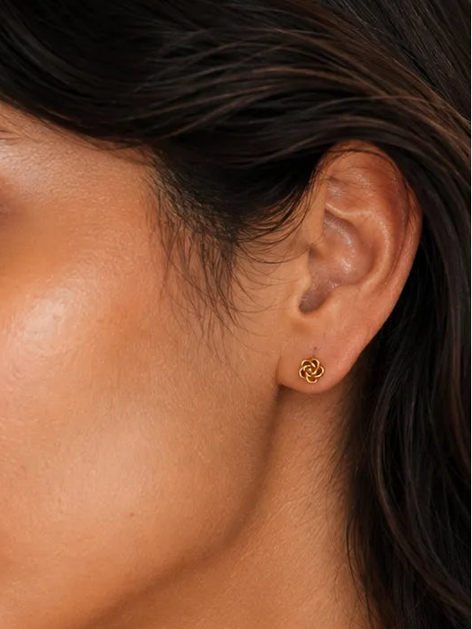 Close-up of a woman wearing a small gold crescent moon stud earring, shown in profile against a warm neutral background.